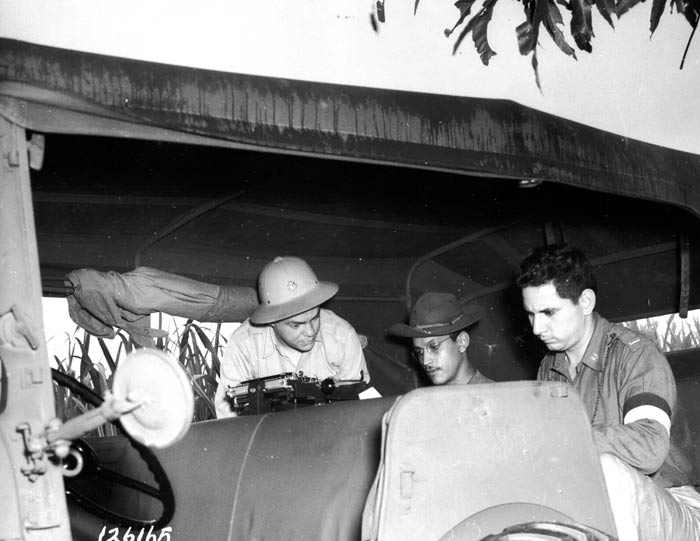 Mr. Samuel Badillo, Publicity Director of the Selective Service, and a guest of the Provisional Maneuver Force, looks on as Sgt Luis F. Rodriguez and 1st Lt. Pedro Pons, Public Relations Officer, work inside a command car. Caguas, Puerto Rico. November 1941.  SC 126165